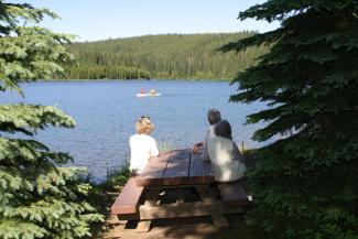 three individuals sitting at picnic table looking out at lake