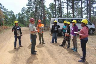 A picture of nine forest workers gathered around a supervisor getting instructions or asking questions.
